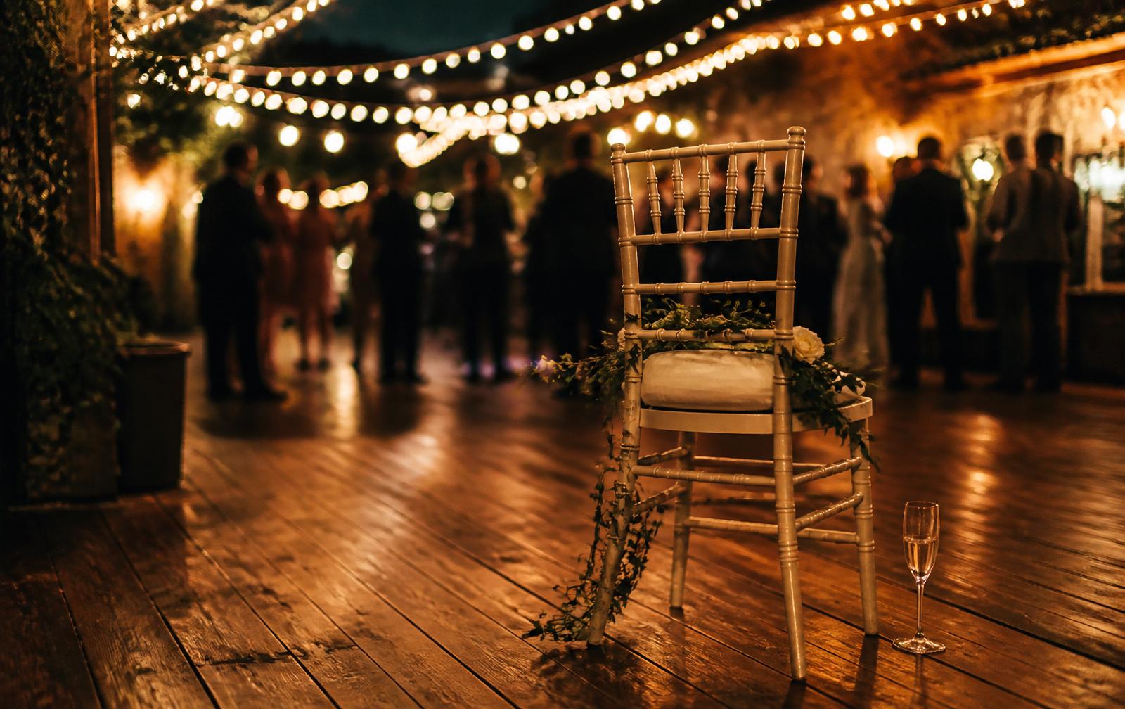 A guest holding a smartphone at a candlelit wedding reception, dancing couples softly out of focus in the background